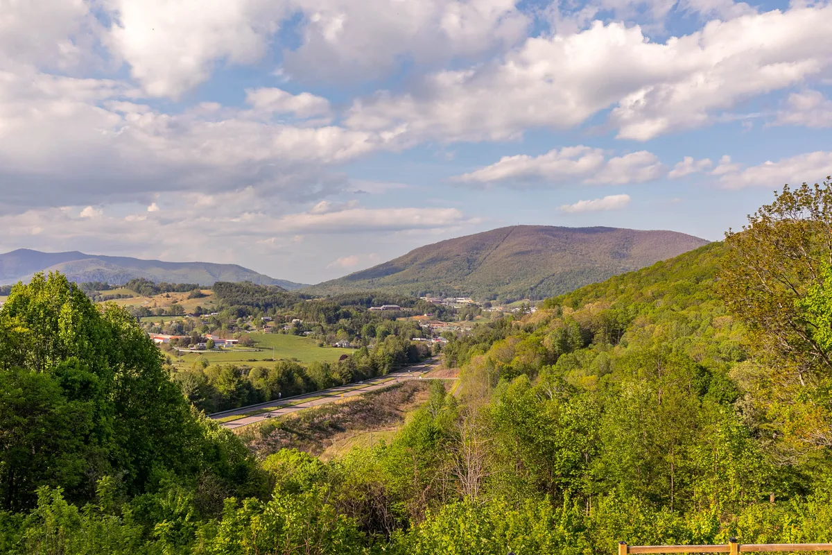 This image captures a peaceful view of lush green mountains with a small town nestled in the valley below. The scene is taken from an elevated vantage point and features a beautiful sunset casting a warm glow over the town and surrounding hills.