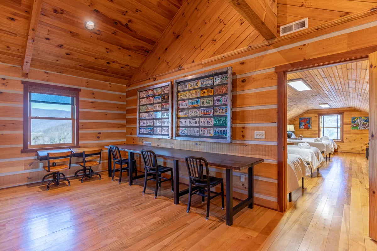 A cozy loft or multipurpose room with wooden tables, creative license plate wall art, and large windows. The room offers a bright, inviting setting ideal for working or studying at the desk, enjoying family game nights, or soaking in natural light. The creative decor adds a playful, energetic vibe.
