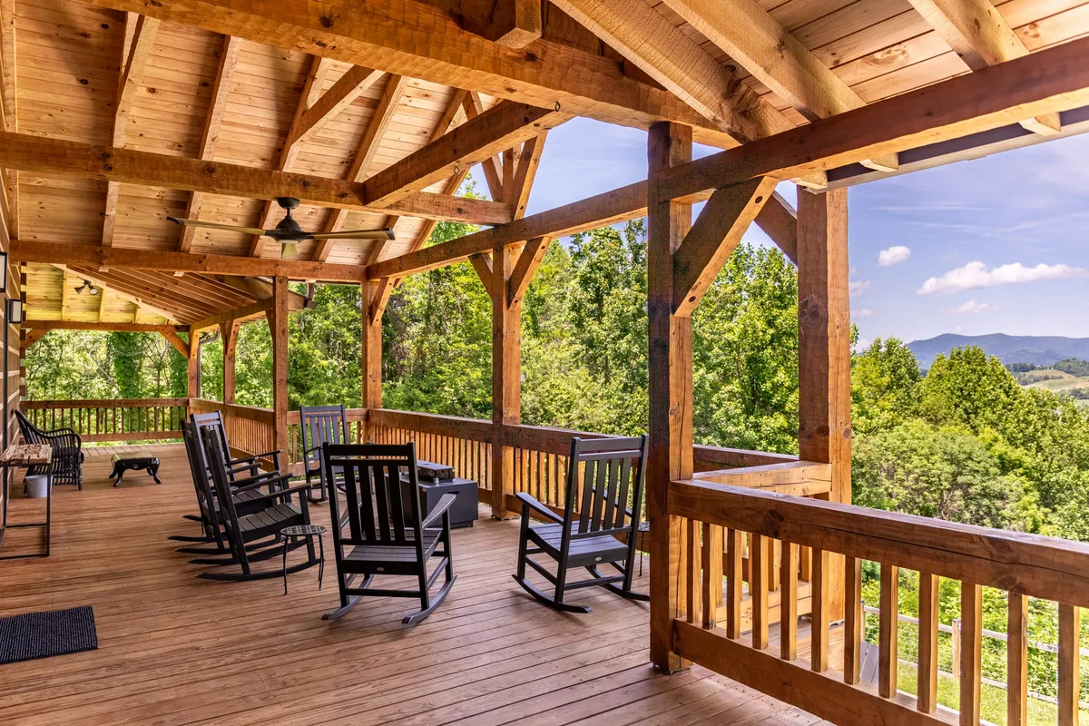 A peaceful exterior porch scene with classic rocking chairs overlooking a sweeping mountain view. Wooden railings frame the view, and the scene suggests a spot to relax and enjoy the surrounding landscape.