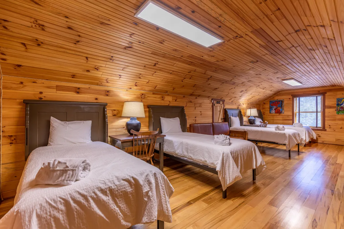 A spacious bunk room with three beds, soft lighting from bedside lamps, a wooden feature wall, and lively wall art. The setup is ideal for children or groups, supporting flexible sleeping arrangements.