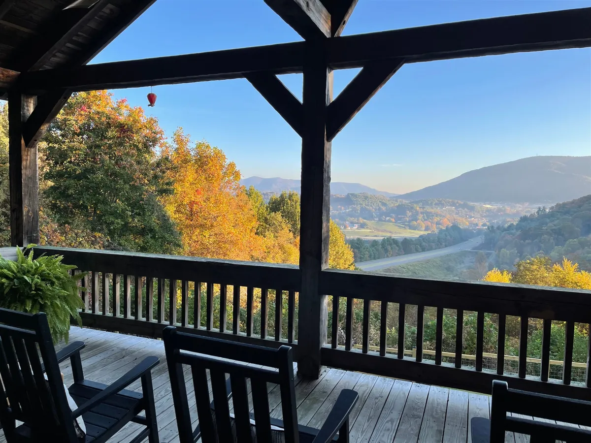 This image shows a pair of classic rocking chairs on a wooden porch, overlooking a landscape of vibrant autumn foliage and distant mountains under a blue sky. The scene conveys a tranquil and inviting atmosphere, ideal for relaxing outdoors while immersed in the beauty of the changing seasons.