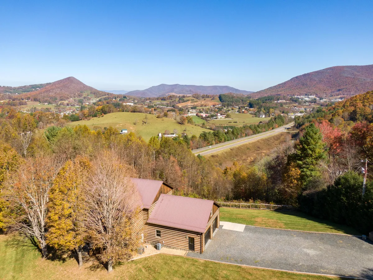 A scenic view of a log cabin nestled among mountains with vibrant autumn foliage. The perspective shows the cabin in the foreground, surrounded by color and natural beauty, hinting at the region's picturesque seasonal changes.