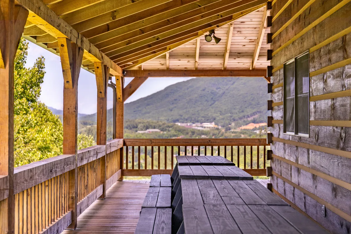 A spacious outdoor porch featuring a wooden table and chairs set against a backdrop of expansive mountain views. The porch is designed for outdoor dining, gathering, or simply enjoying nature, emphasizing community and connection to the landscape.