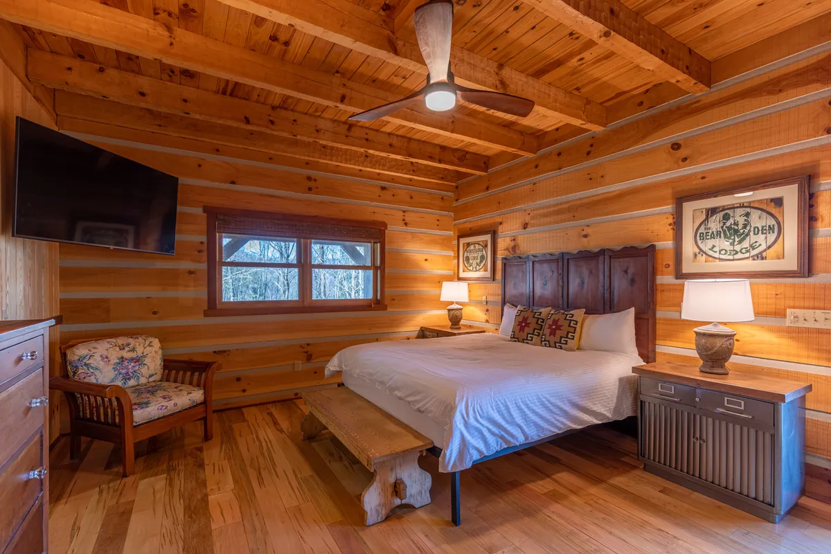 A cozy bedroom with a wooden ceiling, plush bed, wall decor, a comfortable seating area, and warm lighting fixtures. The rustic design exudes comfort and tranquility, suggesting a restful retreat ideal for unwinding. The presence of a TV hints at the private HD TVs mentioned in the section.