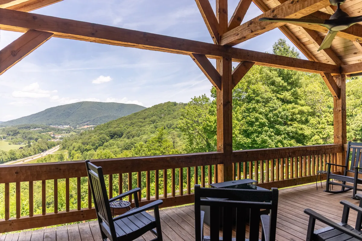 A peaceful wraparound porch with wooden beams, classic rocking chairs, and sweeping mountain vistas in the background. The setting is tranquil, with soft natural light illuminating the outdoor seating—perfect for both relaxation and inspiration during remote work breaks.