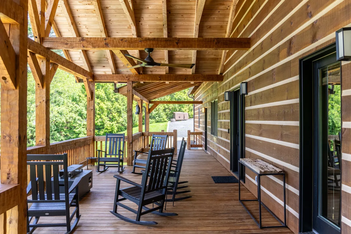 This exterior image highlights a welcoming porch outfitted with rocking chairs, sturdy wooden beams, and a fan overhead, creating an inviting spot to enjoy nature, socialize, or dine al fresco. The view suggests both comfort and scenic outdoor connection for spring and summer activities.