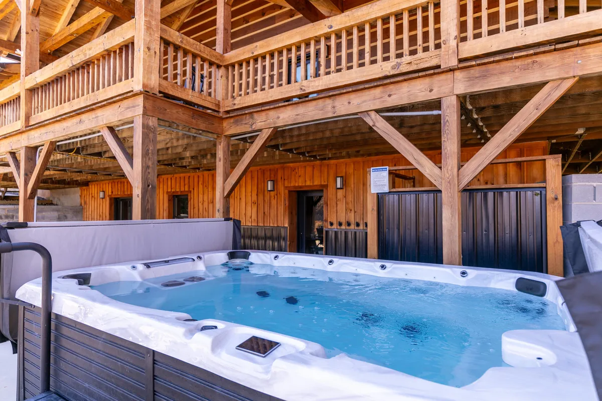 An exterior shot featuring a luxurious hot tub on a wooden balcony, with outdoor seating and a scenic view of the mountains. The setting is perfect for unwinding after a day outdoors, especially during winter with snow-capped vistas or cool evenings in other seasons.