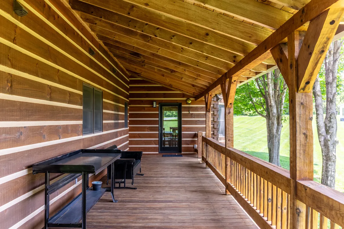 A welcoming wooden porch with log cabin walls overlooks a spacious yard, set against a tranquil natural backdrop. The scene invites relaxation and hints at an expansive outdoor area perfect for pets and their owners.